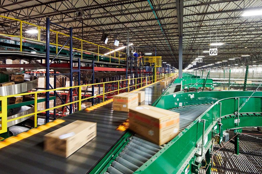 Inside a distribution center: packages moving along a conveyor system beneath
               racking and mezzanine levels.