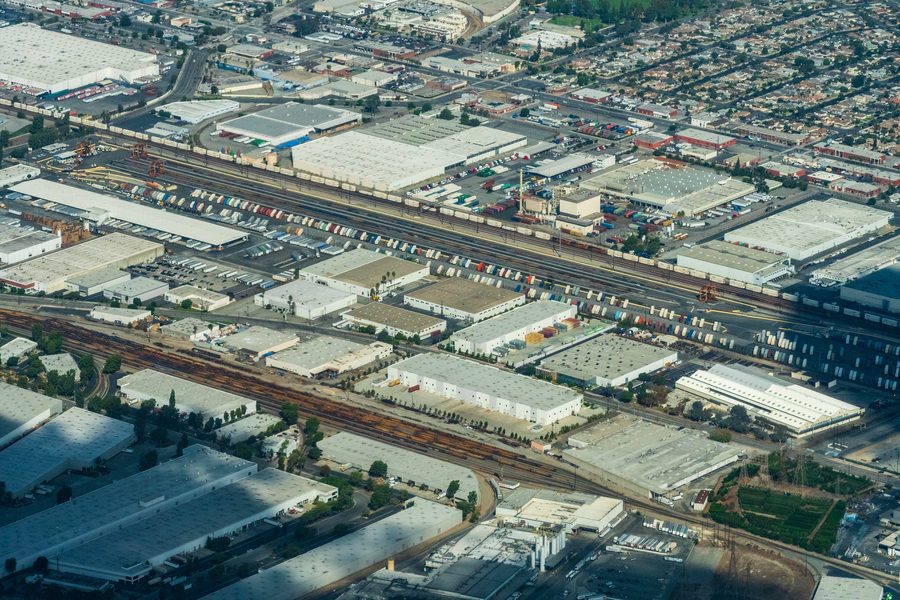 Aerial view of Commerce and Vernon, east of downtown Los Angeles: warehouses,
               truck yards and container stacks packed around the BNSF Hobart intermodal rail
               facility, with freight tracks running through the center and residential streets
               at the edges.
